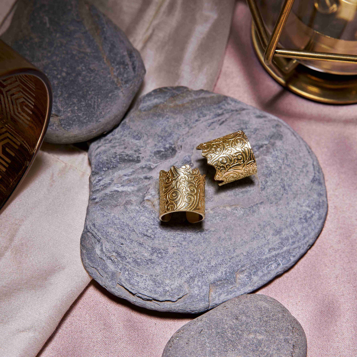 Gold ornate cuffs on a stone surface with a soft pink background