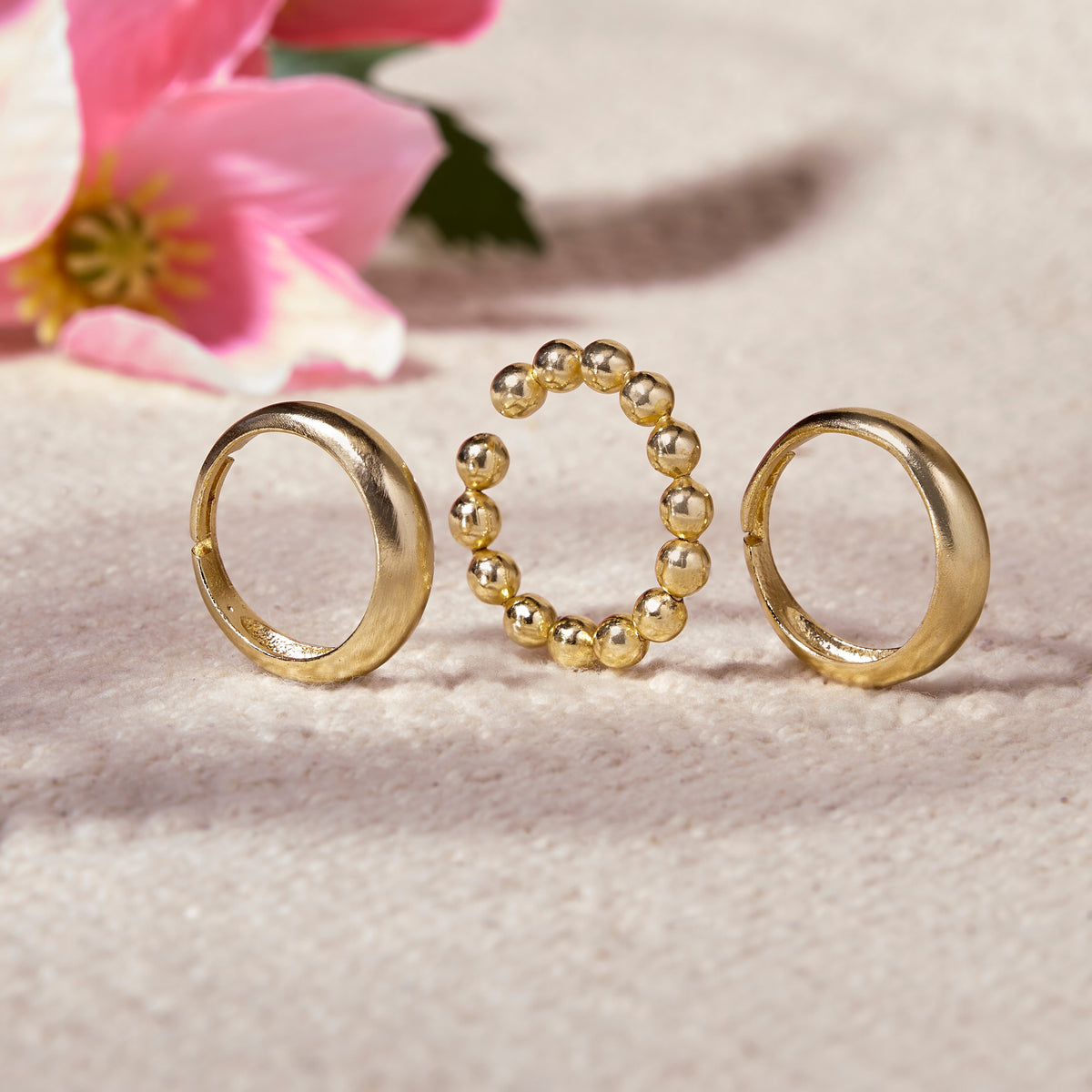 Three gold rings on a textured surface with pink flowers in the background