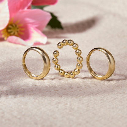 Three gold rings on a textured surface with pink flowers in the background