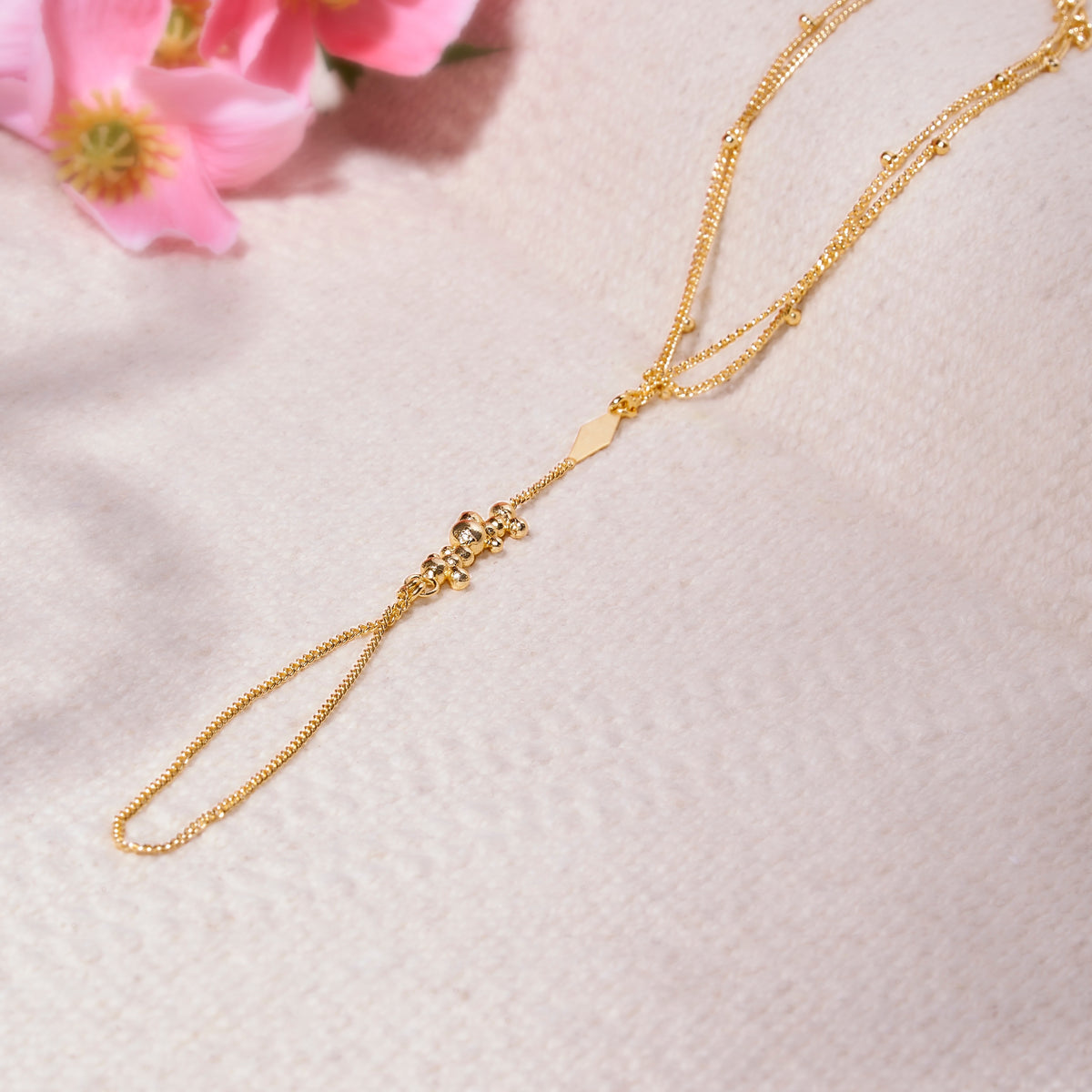 Gold necklace on a light pink textured surface with pink flowers in the corner