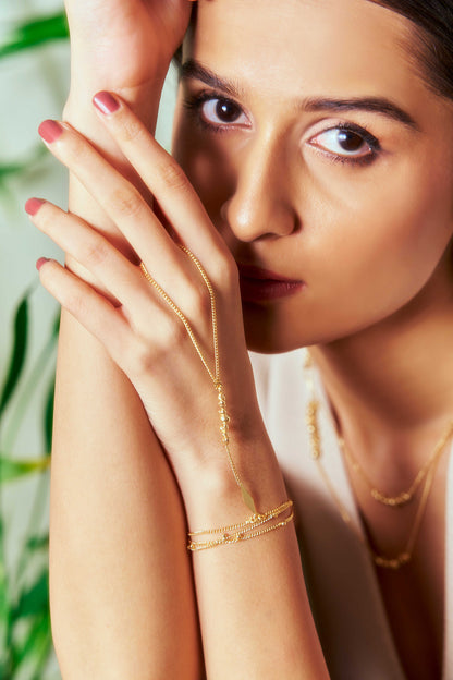 Woman wearing gold jewelry with a blurred green plant background | Molten Hand Chain - Gilded Beads